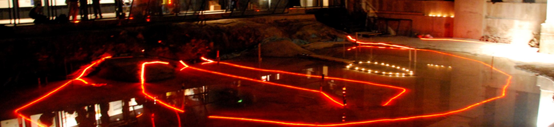 Red lighting shows the outline of archaeological remains of a building preserved beneath a modern development.