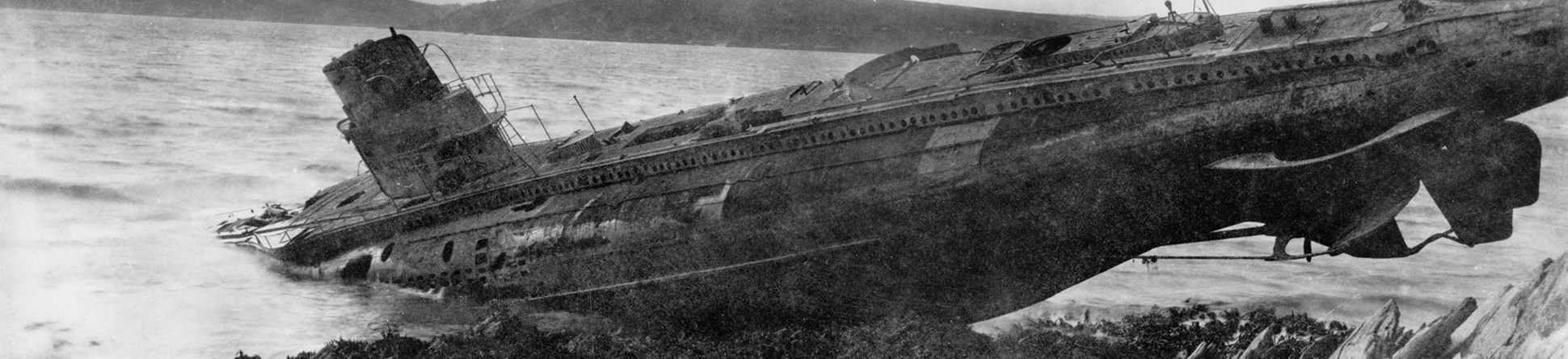 A black and white archive image of a submarine stranded on a rocky coast.