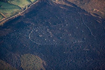 Aerial photograph of a Prehistoric enclosure and cairnfield in a moorland landscape that has been burned by fire.