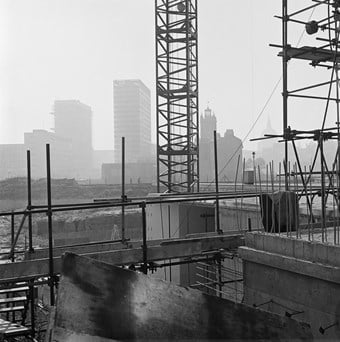 A black and white photo showing the Barbican Estate under construction. Cranes and scaffolding are in the foreground, while St Giles church and the dome of St Paul’s Cathedral are visible in the background.