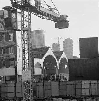 A black and white photo showing Liverpool Street station with a crane in the foreground. Tower blocks of the barbican can be seen under construction in the background.