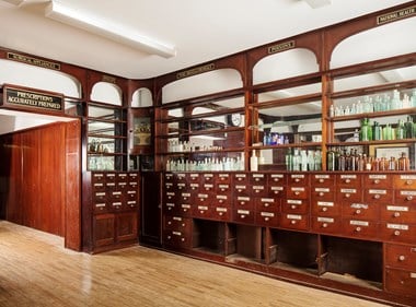 Interior of chemist shop with original wooden drawers and shelves displaying glass bottles.