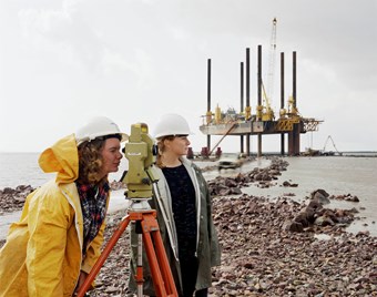 Two female Laing employees use a theodolite in front of the 'Jay Robertson' barge in the River Severn.