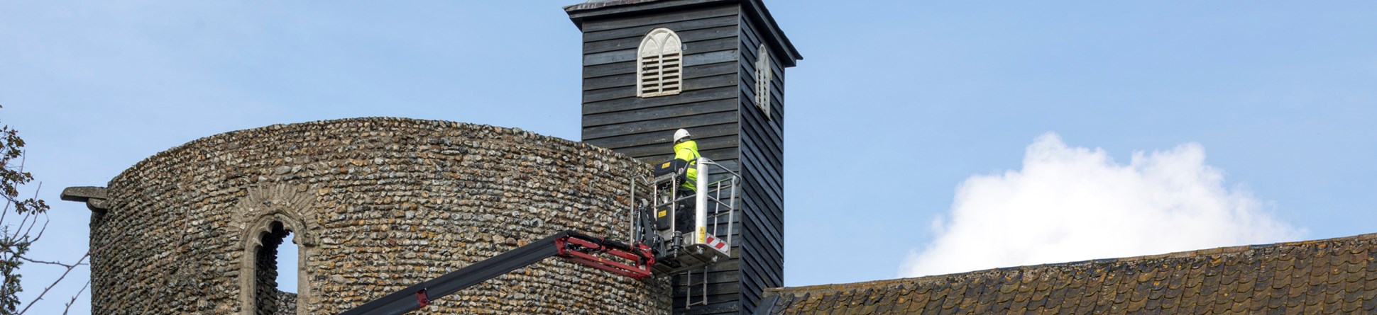 A man in high-vis jacket and hard hat works on the tower wall from a cherry picker.