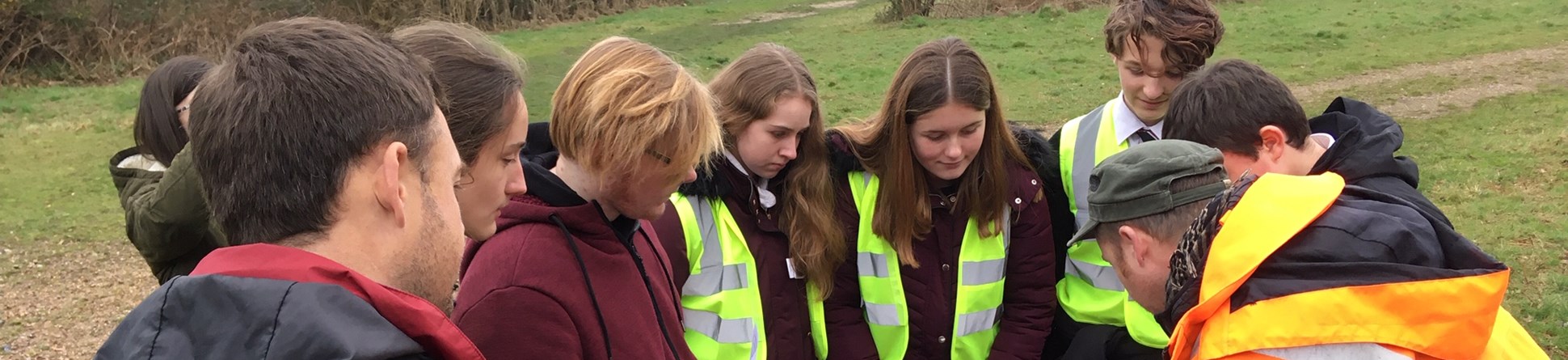 A group of secondary school pupils and their teacher look at a site plan with an archaeologist.