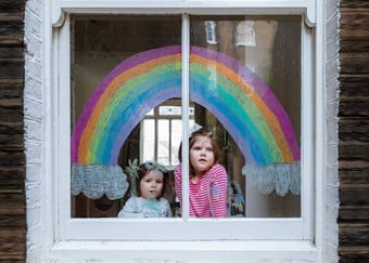 Two young girls sit beneath a rainbow painted on their front window