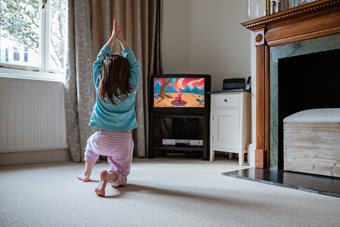 A young girl follows a children’s yoga video in the living room