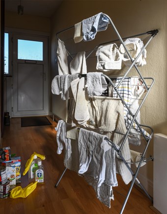 Baby clothes dry on a plastic clothes horse beside disinfectant products in a modern hallway.