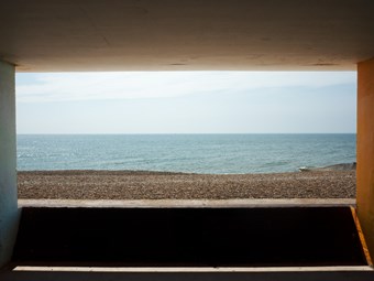 A view out to sea on a pebbly beach is framed by four concrete walls of a promenade.