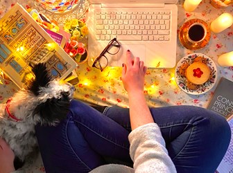 Overhead view of a person sitting cross-legged on the floor in front of a laptop surrounded by lights and candles