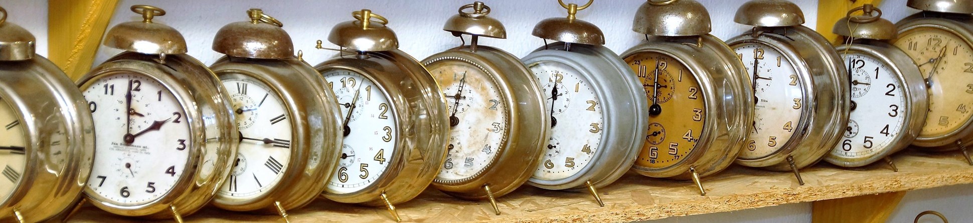 Image of old fashioned brass alarm clocks on wooden shelves.