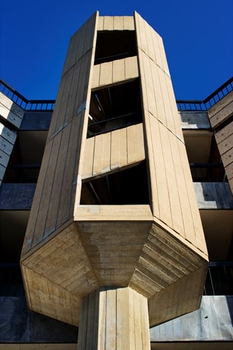 An octagonal stair turret in a gap on the front of a Brutalist university building.