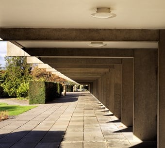 Low sun shining on a paved walkway. The raised ground floor allowing the ground underneath to be used - one of Le Corbusier’s main features of Modernism.