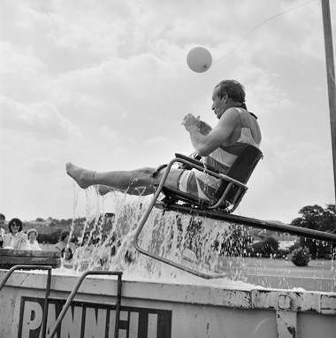 A man in a dunking chair, being raised from a water-filled skip, as part of the 'dunk-a-director' game