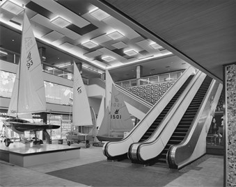 Black and white photograph of the Centre Court at the Bull Ring shopping centre. Three large sailing boats are on display next to a pair of escalators.