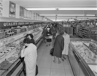 Black and white photograph showing the interior of the Fine Fare supermarket at the Bull Ring shopping centre. Shoppers are browsing the aisles; some carrying shopping baskets. The dairy aisle is in the foreground of the photo.
