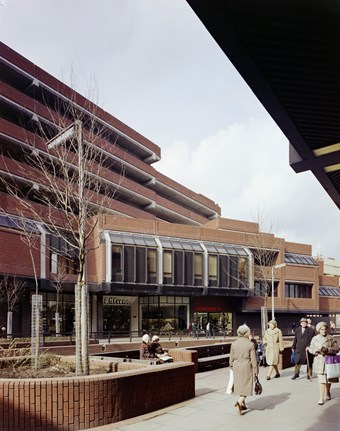 Colour photograph showing part of Wood Green Shopping City from the street. There are shops fronting High Road, including a D H Evans store, and people strolling past in the foreground.