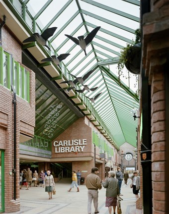 Colour photograph taken from one of the glass covered lanes at The Lanes Shopping Centre, looking towards Carlisle Library. Suspended from the roof above are a group of glass fibre birds.