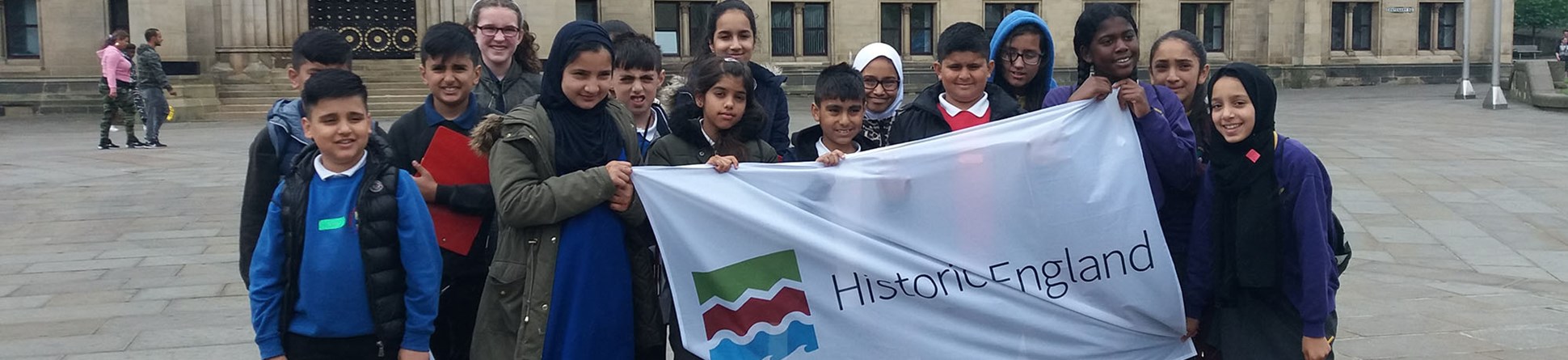 Pupils outside Bradford City Hall holding a banner with the Historic England logo on it.