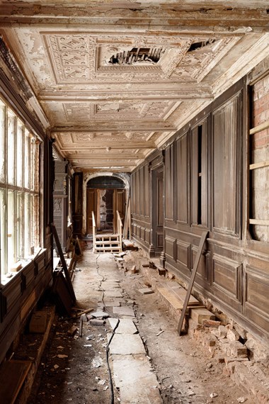 View down a long wood panelled gallery with extensive damage.