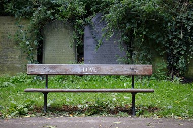Bench with freshly sprayed grafitti saying 'Love' in front of gravestones.  View from east.