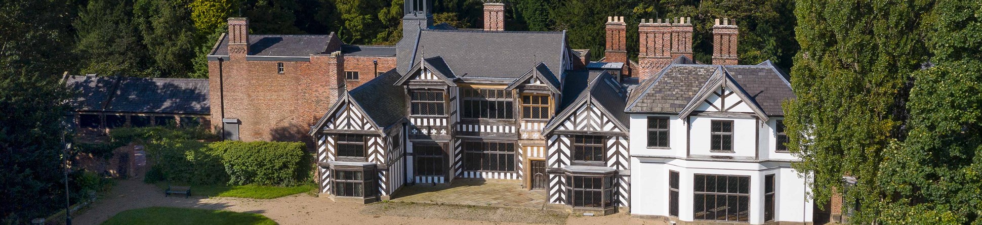 Exterior, east elevation, drone image showing hall after conservation/ restoration work following the arson attack in March 2016. View from east. 16th century stately home with lawns and gravel in foreground. Woods in background.