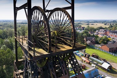 Colour photo of pit headgear mounted on top of Astley Colliery with view over houses and countryside behind.