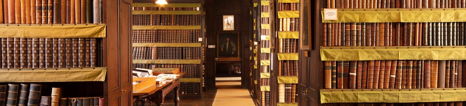 rows of dark wood historic bookcases line the Plume Library, filled with classic leatherbound books against a wooden timbered flooring lightened by a pale cream carpet runner.
