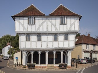 a pale timber framed building with red brick roof and ground floor arches on a cobbled street immediately facing the road.