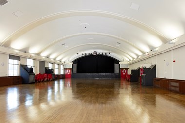 View up the length of a large ballroom with highly-polished wooden floor, white walls and slightly domed ceiling.