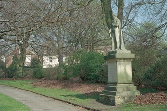 Statue on the right, to one side of a path leading to the left, bordered by trees.