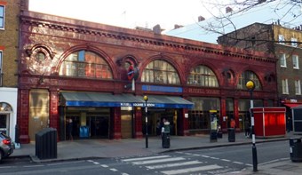 Red-tiled exterior of underground station viewed across a road with pelican crossing in foreground.