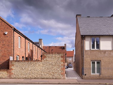 The end of a terrace of residential buildings with a flint and brick boundary wall and alleyway between houses.