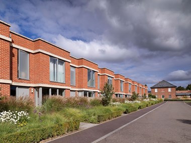 A terrace of modern flat roofed brick dwellings with an older brick building in the background.