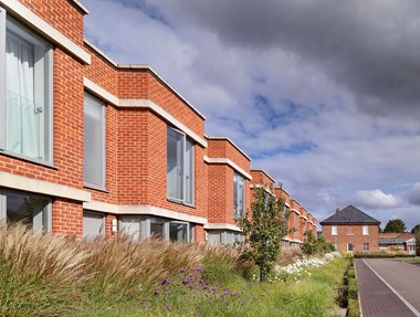 View of a terrace of new two-storey brick housing with flat roofs, with older brick buildings in the background.