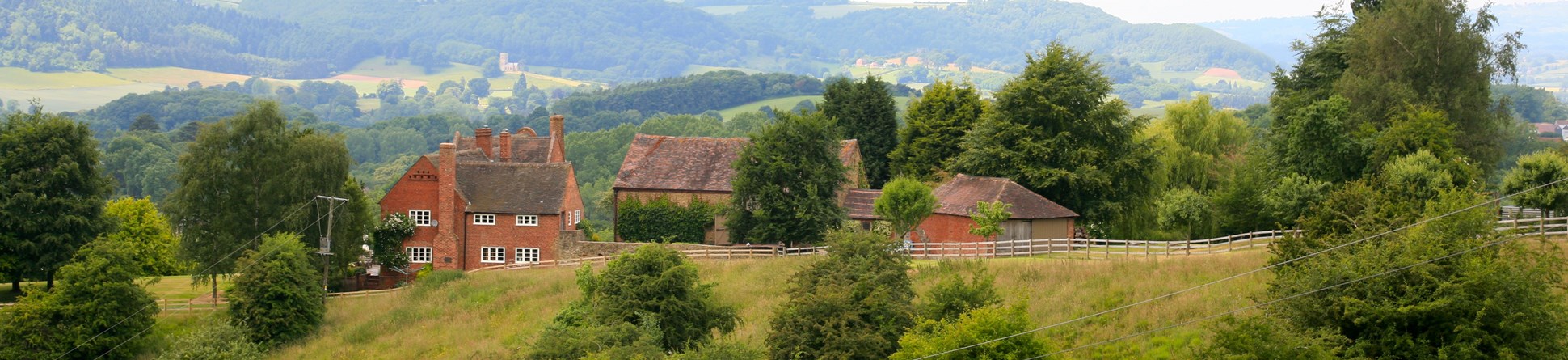 Traditional red brick house and farm buildings set in rolling countryside.