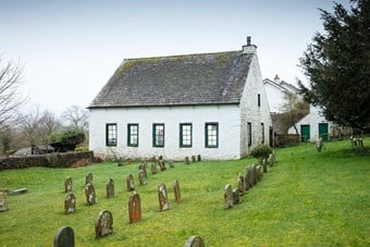 Stone whitewashed building with gravestones in foreground
