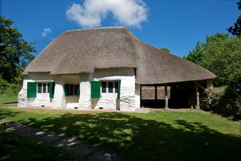 Thatched whitewashed stone building with green shutters on the windows