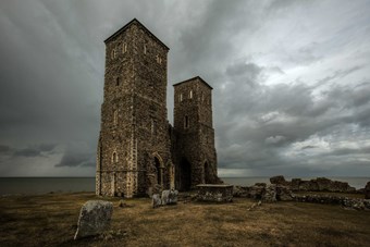 Twin tower remains of Reculver parish church surrounded by dark clouds