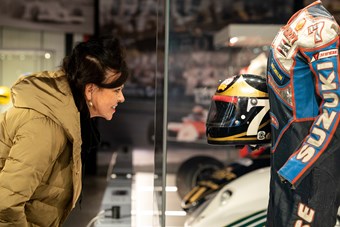 Woman looking at professional motorcycle racer Barry Sheene's leathers and helmet behind a glass screen.