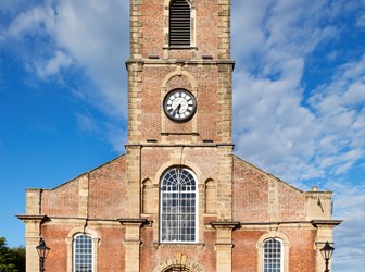 The front elevation of a church made of brick. There is a clock in the middle of the tower. 