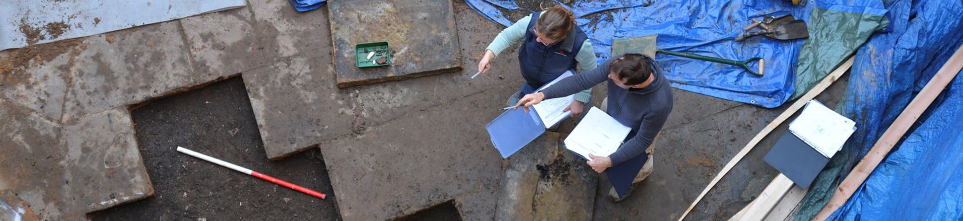 A view looking down into the interior of the tower, showing two archaeologists discussing and recording the trench in front of them.