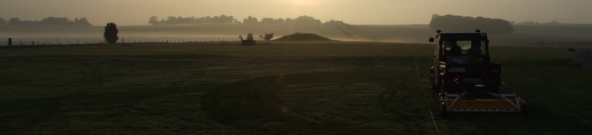 Colour photograph showing a misty landscape with a small buggy towing a low yellow "truck" near the right hand edge