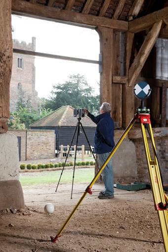Colour photograph of a man setting up a laser scanner with target on a tripod in the foreground and church in the background