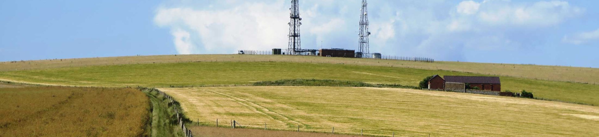 A landscape with fields, farm buildings and telecommunications masts.