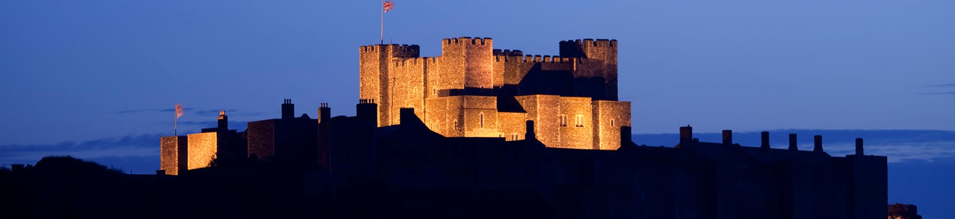 A large medieval castle keep dramatically floodlit at twilight.