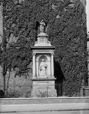 Black and white photo of a white monument next to a building wall covered in ivy