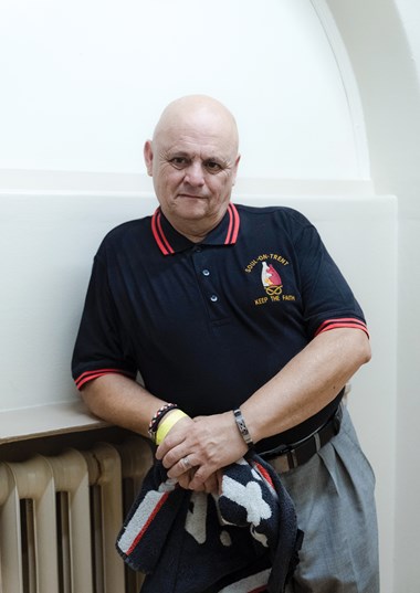 A man in a "Soul-on-Trent - Keep the Faith" Polo shirt leans against a radiator.