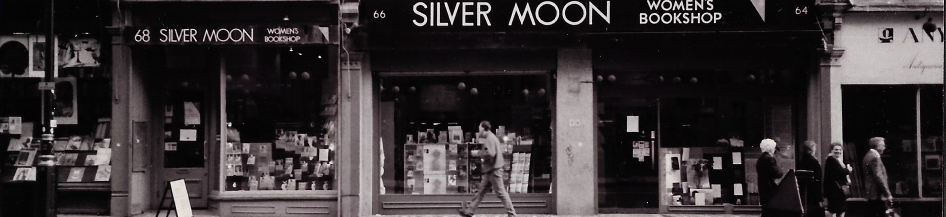 Black and white photo of the front of the Silver Moon Bookshop photographed from the street with pedestrians walking past.