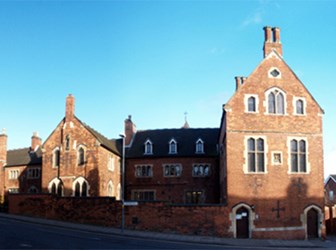 A large red brick building with multiple chimneys on a sloping residential street.